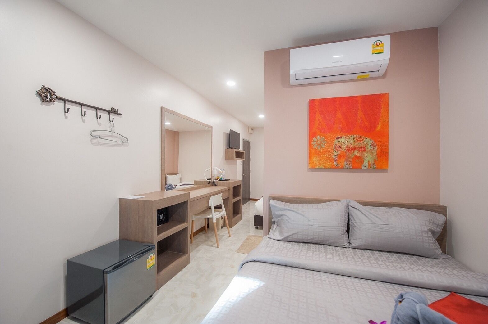 Quarto de hotel com cama, escrivaninha com cadeira, guarda-roupa, espelho, ar condicionado e uma obra de arte na parede.