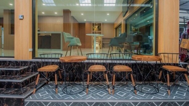 A modern cafe with a glass wall, wooden tables, and metal chairs. - The Moon Night Hotel (Bangkok)