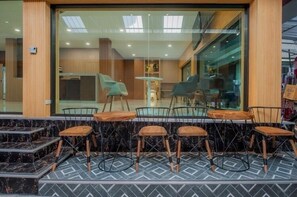 A modern cafe with a glass wall, wooden tables, and metal chairs. - The Moon Night Hotel (Bangkok)
