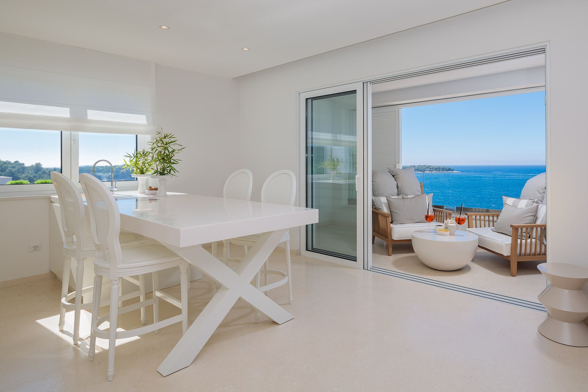 A modern interior with a dining area, a seating area with a view of the sea, and a large sliding glass door.