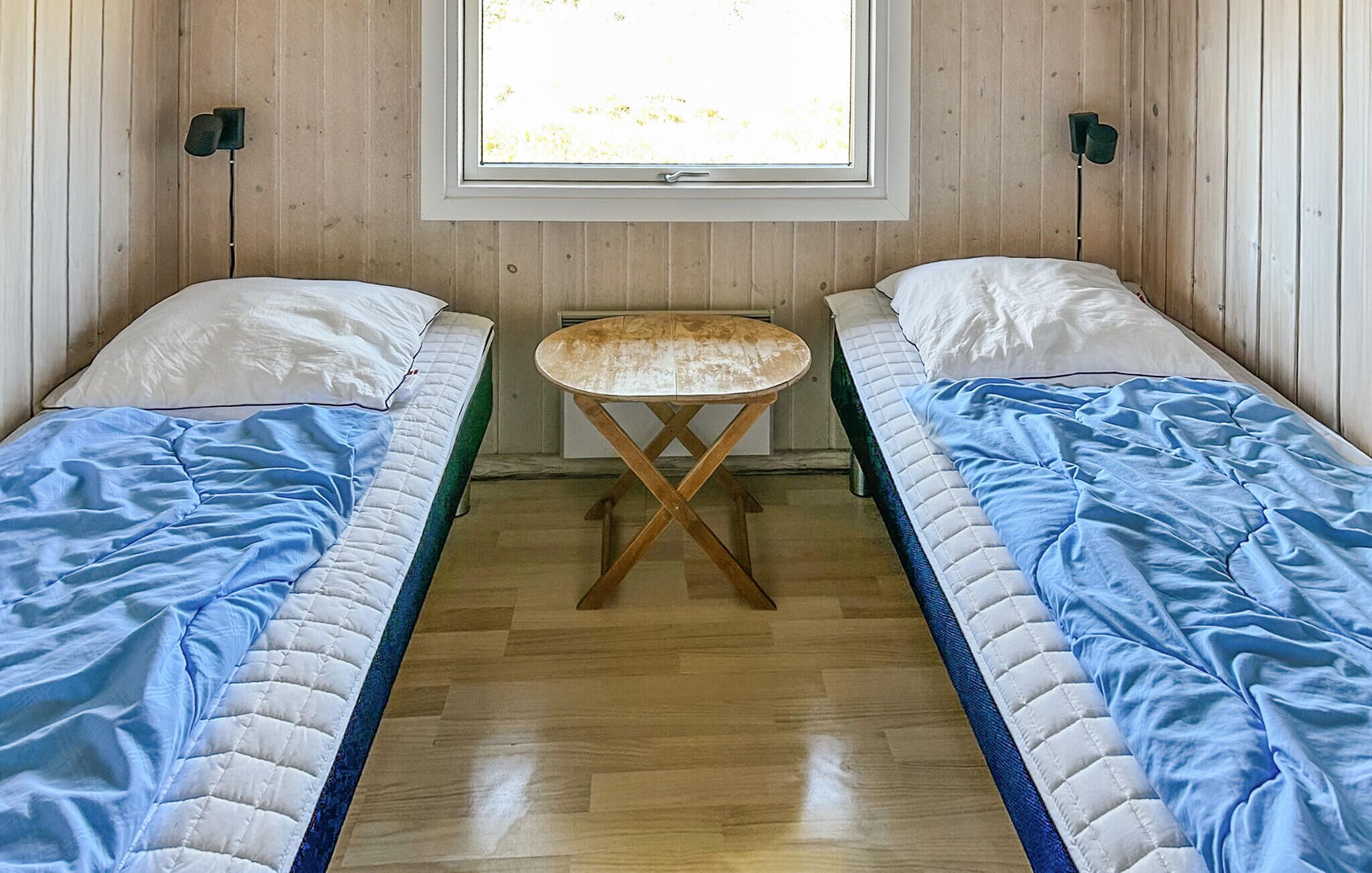 Une chambre avec deux lits simples, une petite table en bois et une fenêtre donnant sur des arbres.