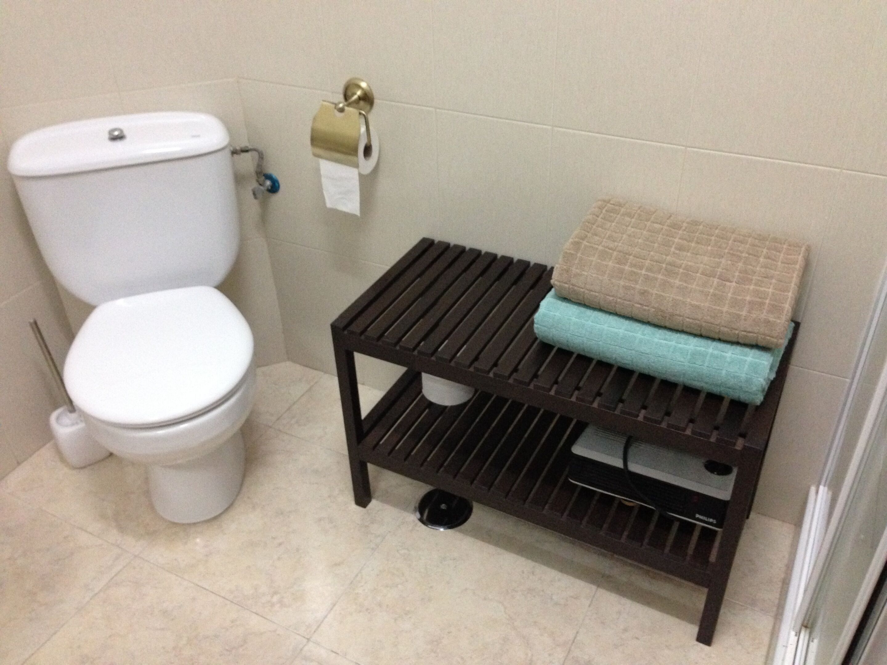 A bathroom with a toilet, a toilet paper holder, and a shelf with folded towels.