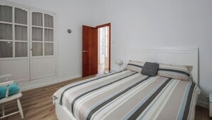 Un dormitorio con cama, una silla, un armario y una puerta que da a otra habitación.