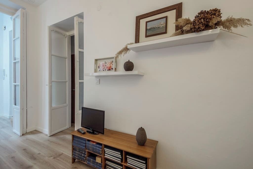 A room with a TV on a wooden stand, a bookshelf, and a door leading to another room.