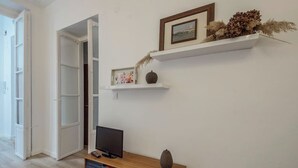 Una habitación con una televisión sobre un mueble de madera, una estantería y una puerta que da a otra habitación.