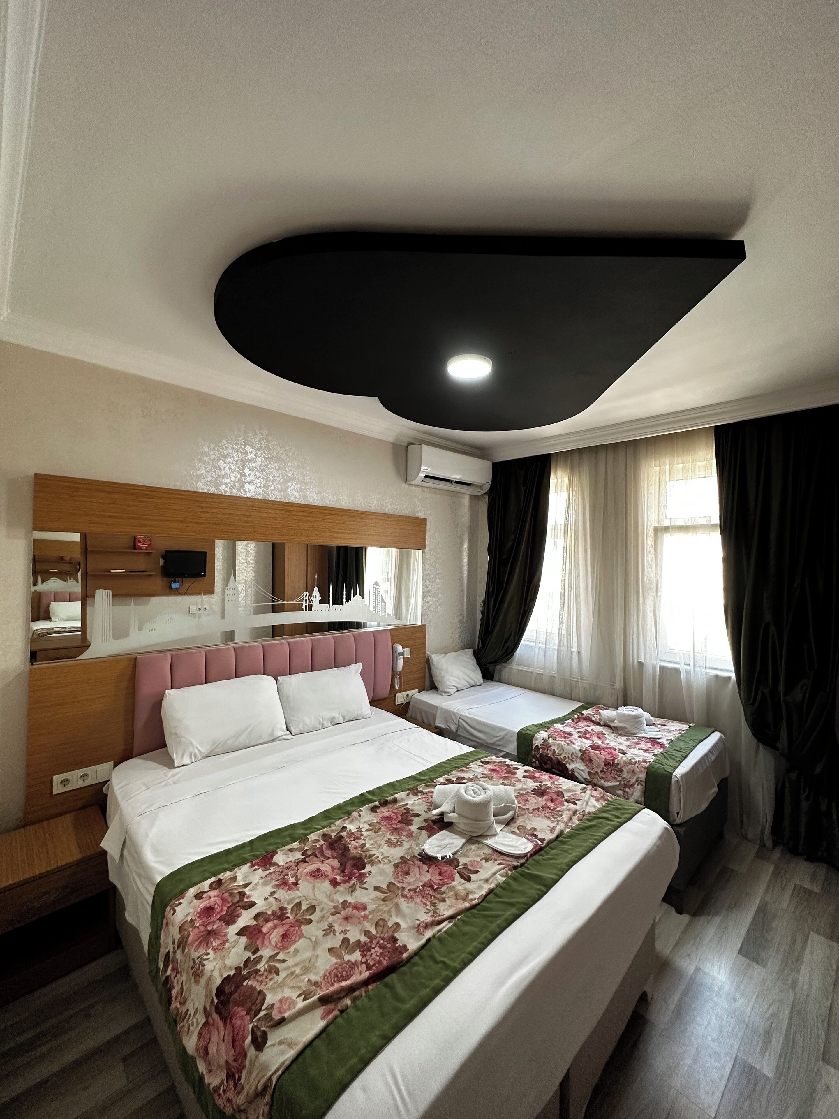 A hotel room with two beds, a large mirror, an air conditioning unit, and a window with curtains.