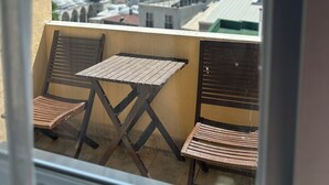 Un balcón con dos sillas de madera y una mesita, con vista a un paisaje urbano que incluye una mezquita destacada y una masa de agua.