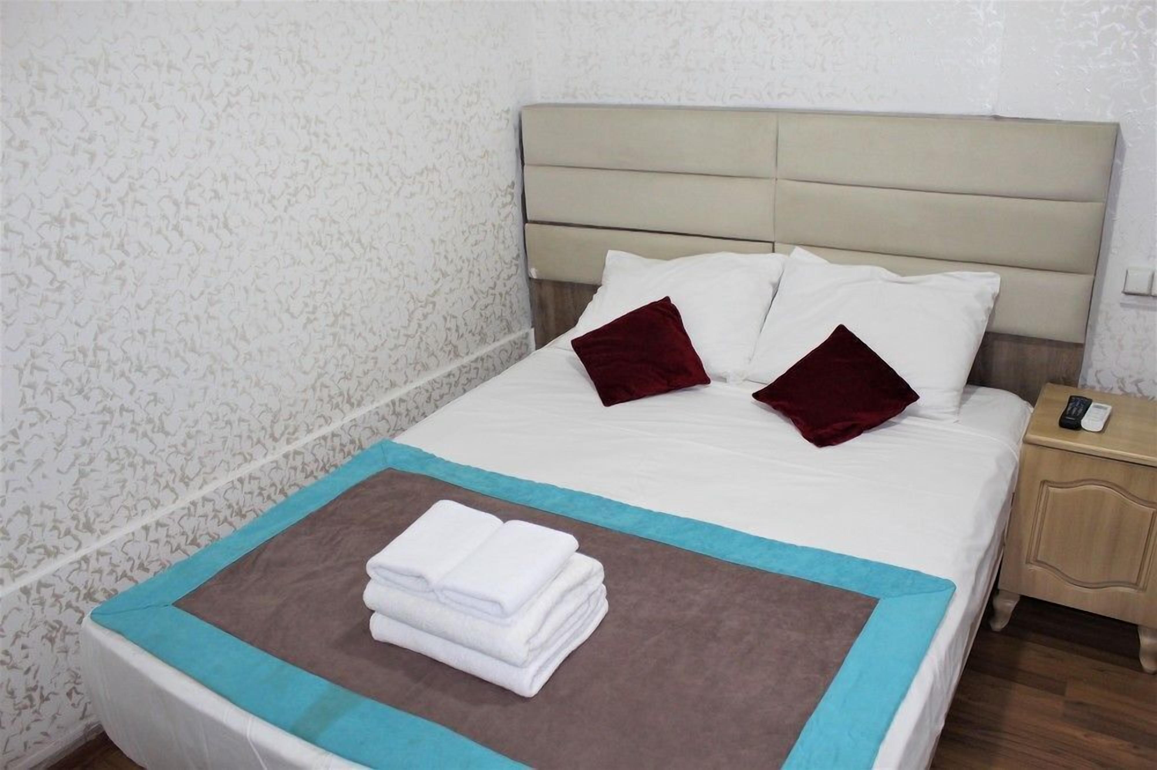 Un lit bien fait, avec des oreillers blancs et bordeaux, une serviette blanche pliée et un motif marron et bleu sur la couvre-lit.