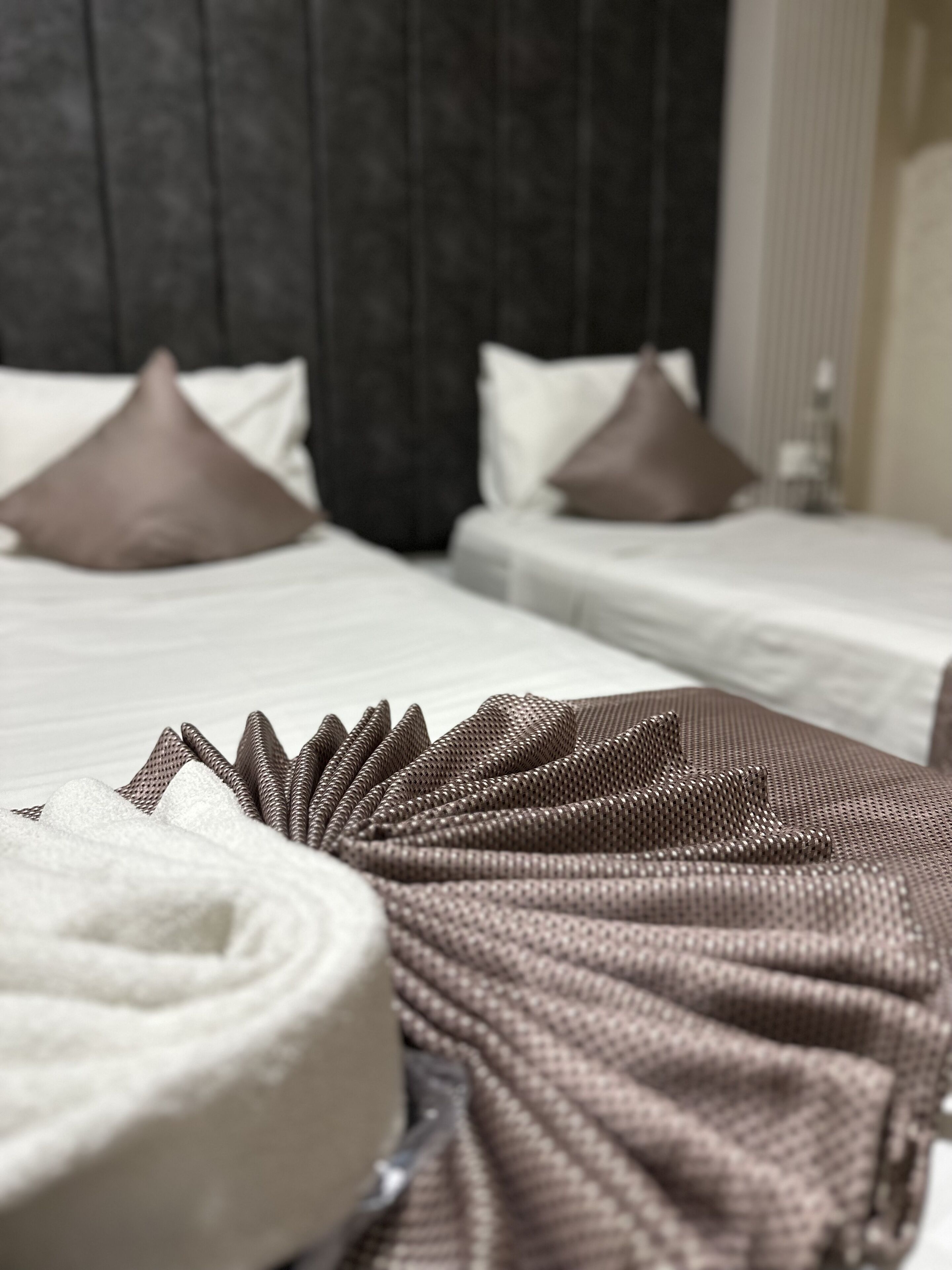 Una camera d'albergo con due letti, ciascuno con copripiumino bianco e cuscini marroni. Una coperta marrone e strutturata è adagiata sul letto in primo piano.