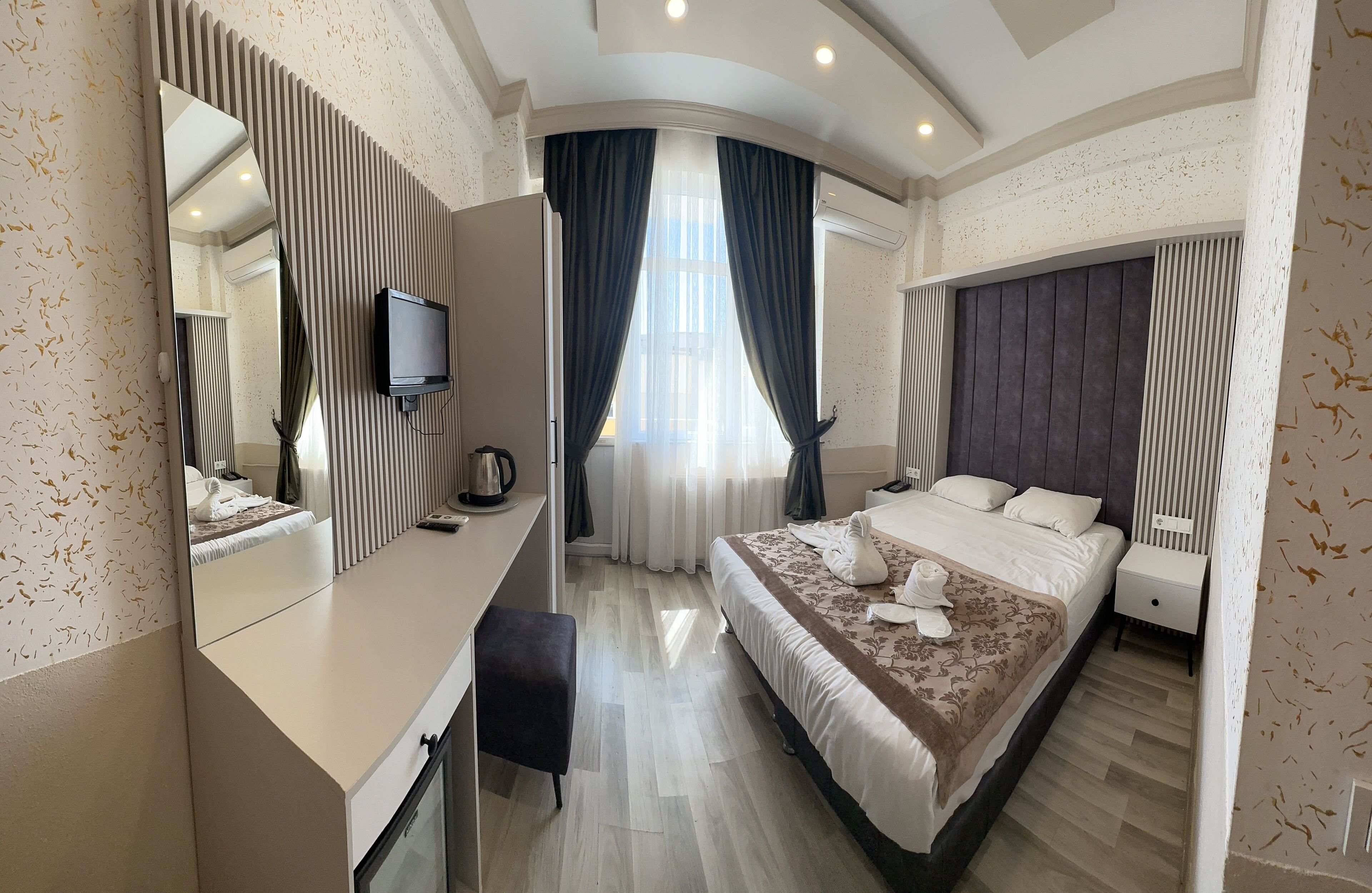 A hotel room with a bed, a desk, a TV, and a large mirror.