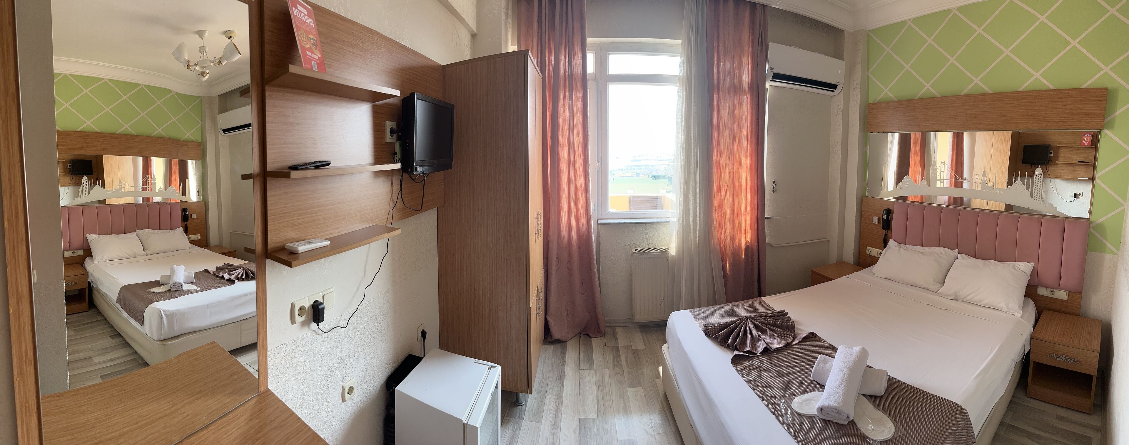 Habitació d'hotel amb dos llits, televisió, minibar i una finestra gran amb cortines.