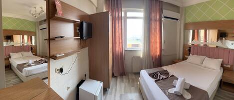 A hotel room with two beds, a TV, a minibar, and a large window with curtains.