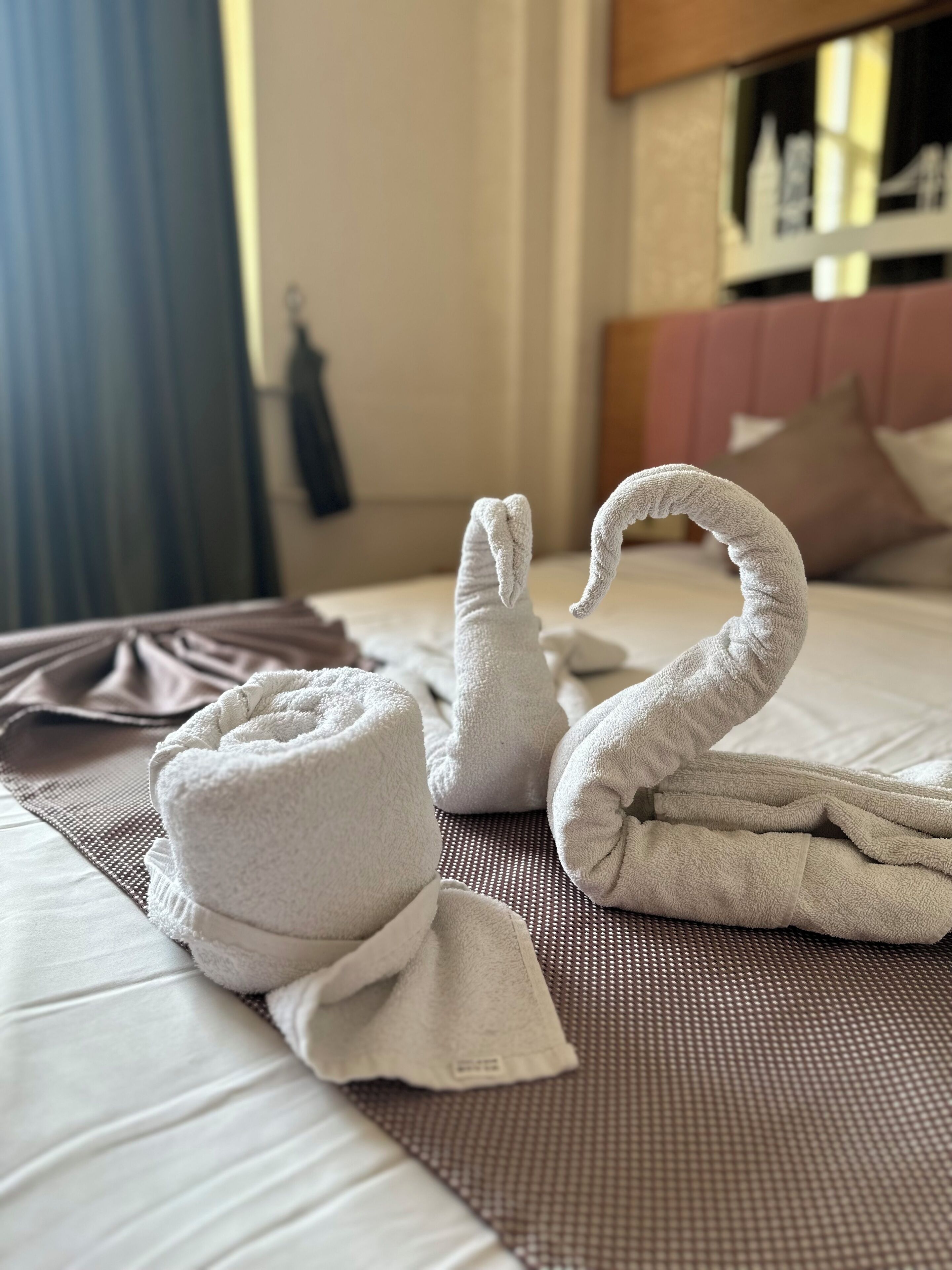 A neatly made bed with a swan towel design, a folded towel, and a brown mat.