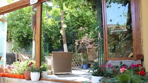 Un patio con plantas en macetas, una silla de mimbre y un muro de piedra.