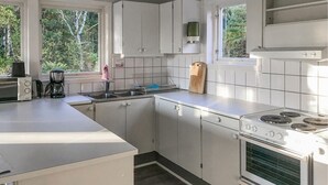 Eine moderne Küche mit weißen Schränken, einem Herd, einer Spüle und einem Fenster mit Blick auf Grünflächen.