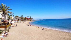 A beach with palm trees, a clear blue sky, and a calm sea.