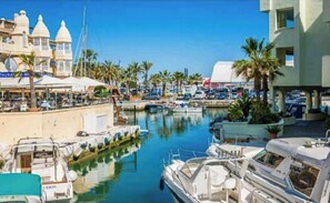Un port de plaisance avec des bateaux amarrés, un restaurant doté d’une terrasse, et un bâtiment à la façade blanche.