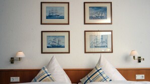 Een hotelkamer met twee bedden, elk met hoofdbord en kussens. Er hangen vier ingelijste nautische schilderijen aan de muur.