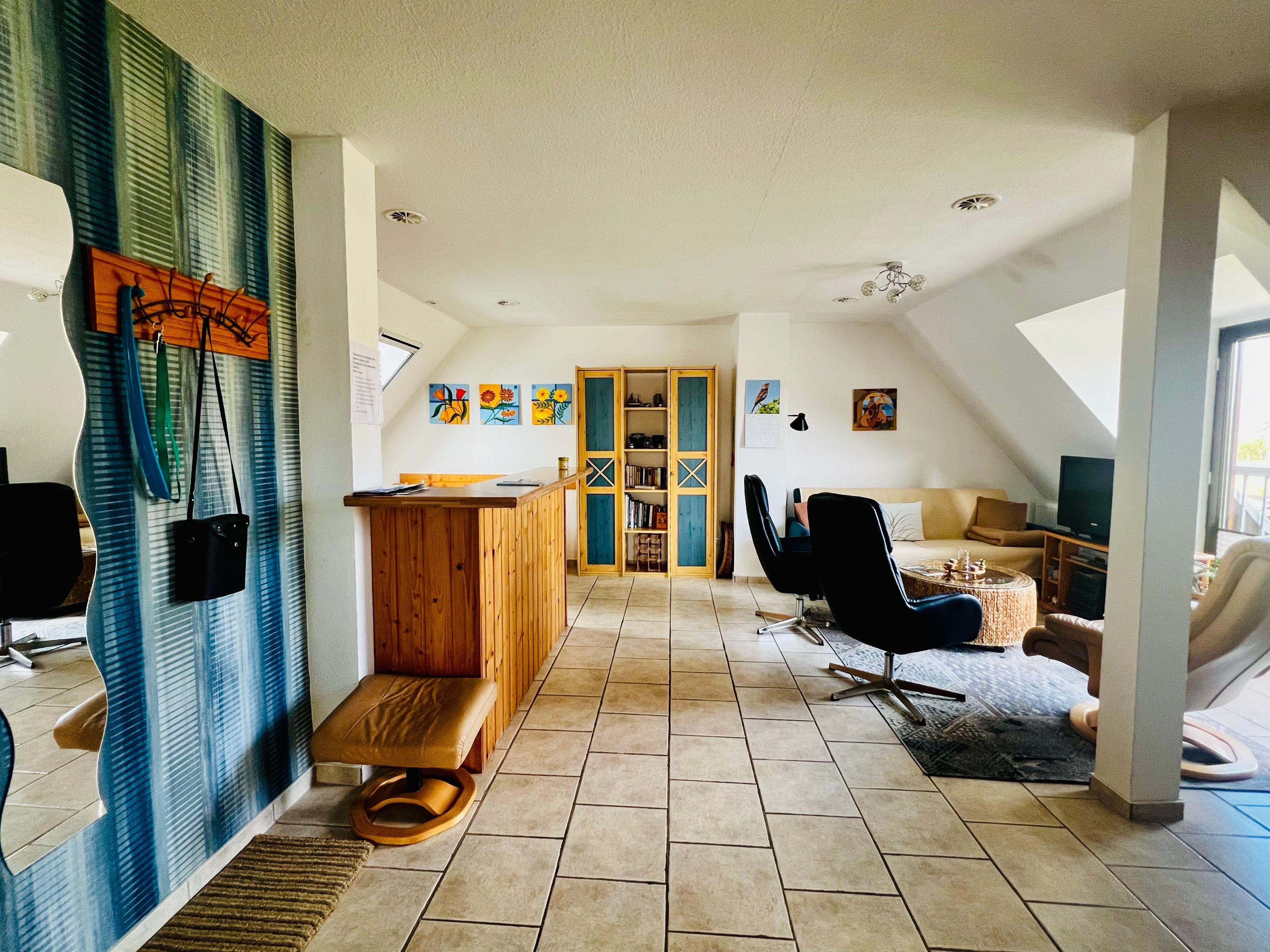 A spacious loft with a high ceiling, a wooden reception desk, a seating area with a sofa and chairs, a television, and a large window.