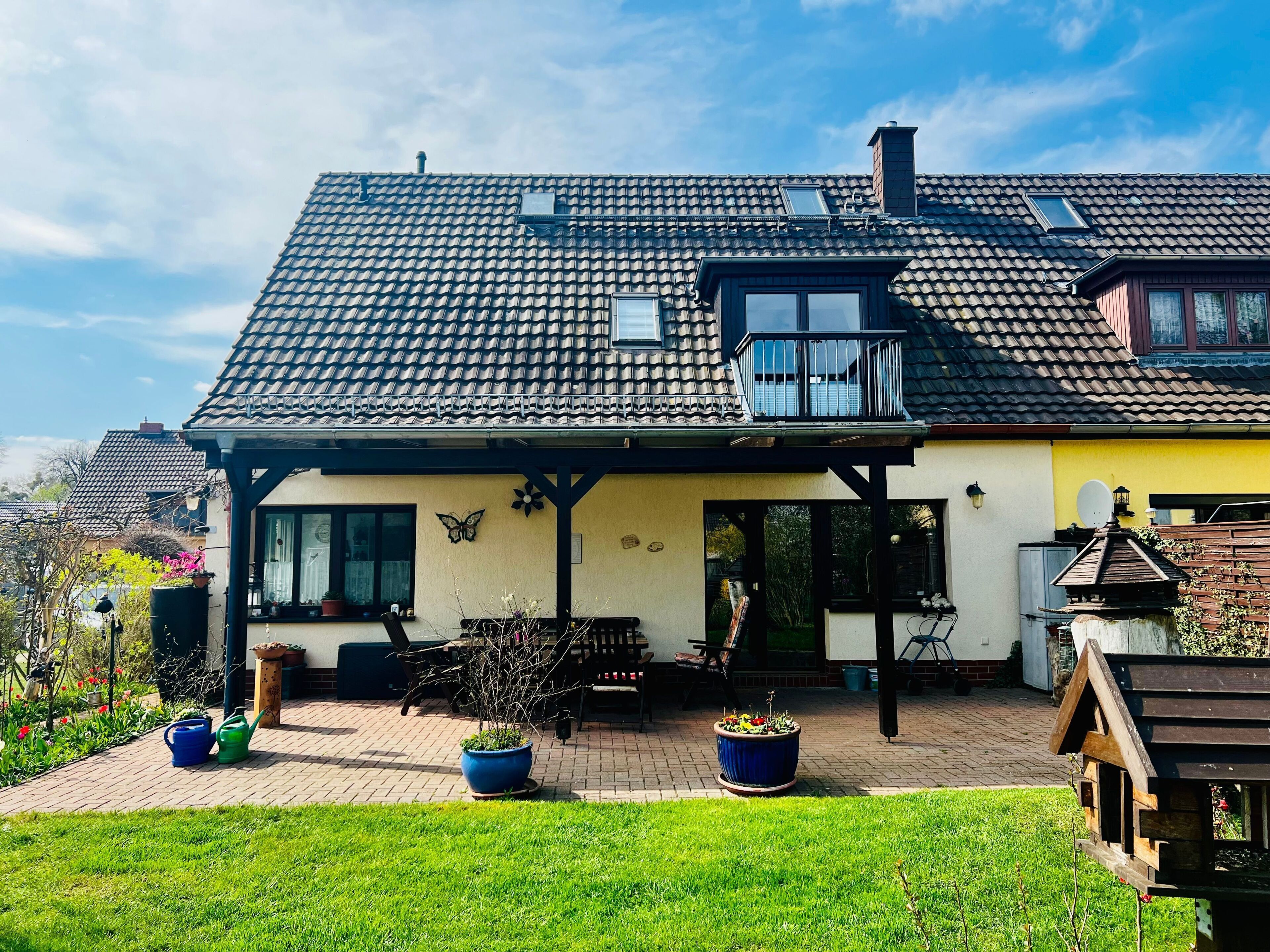 A two-story house with a tiled roof, a balcony, and a garden area with potted plants.