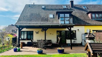 A two-story house with a tiled roof, a balcony, and a garden area with potted plants.