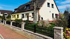 A two-story house with a sloped roof, a visible chimney, and a front yard with a black metal fence. - Vacation apartment Baum - Holiday apartment (Rechlin)