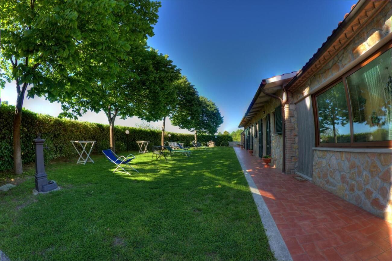 A house with a stone exterior, a paved pathway, and a well-maintained lawn with two lounge chairs.
