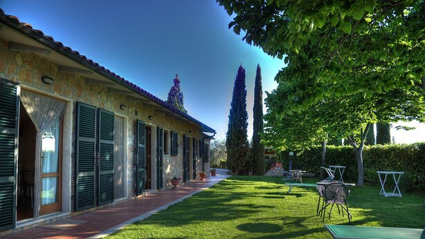 A stone building with shutters, a paved walkway, and a well-maintained lawn with outdoor furniture. - Agriturismo Poggio del Drago (Manciano)