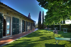 A stone building with shutters, a paved walkway, and a well-maintained lawn with outdoor furniture. - Agriturismo Poggio del Drago (Manciano)