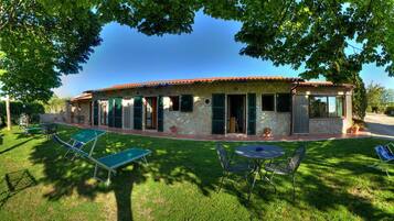 A house with a stone facade, green shutters, and a patio with outdoor furniture.
