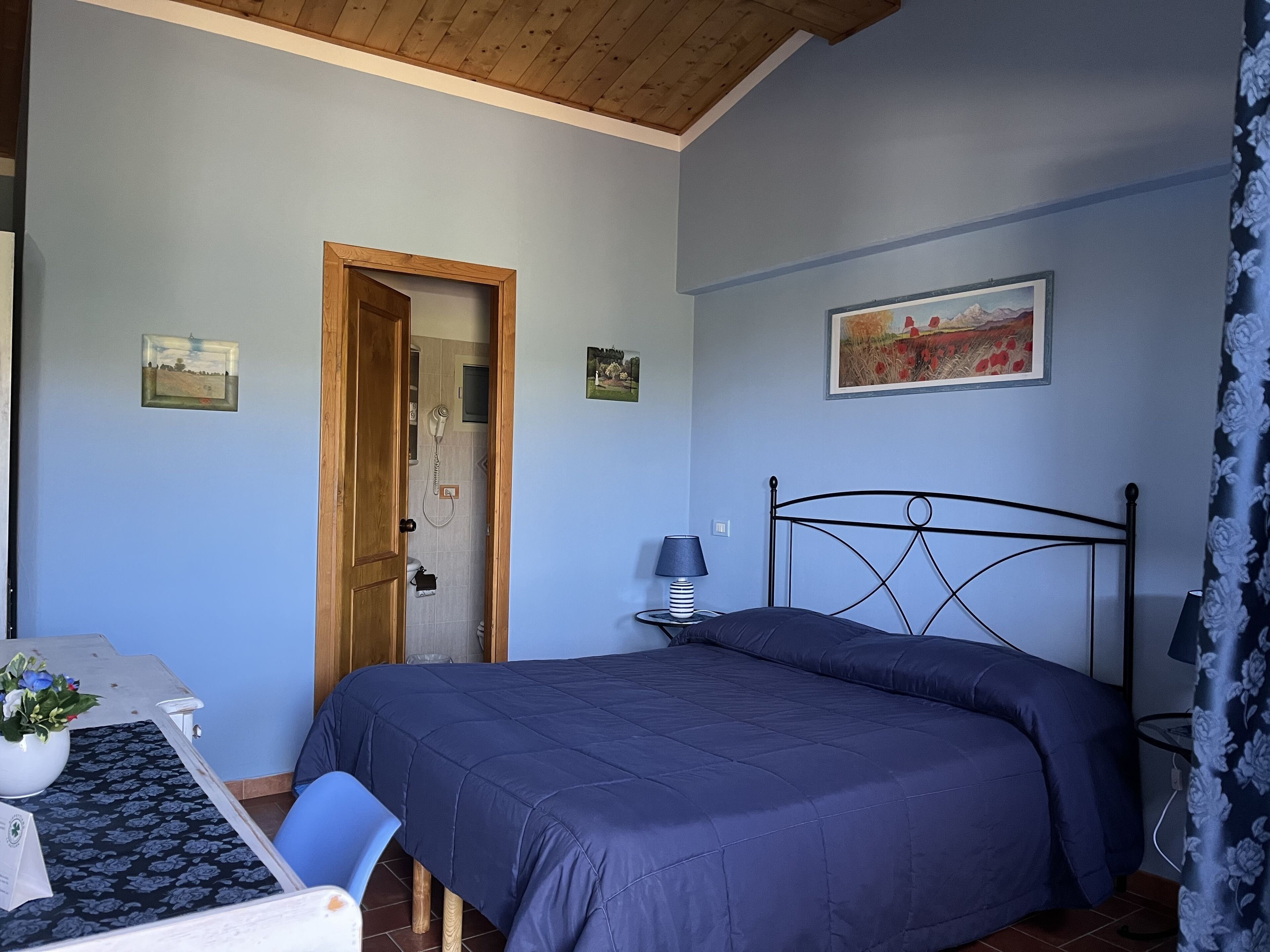 A bedroom with a bed, a desk with a chair, a lamp, and a door leading to a bathroom.
