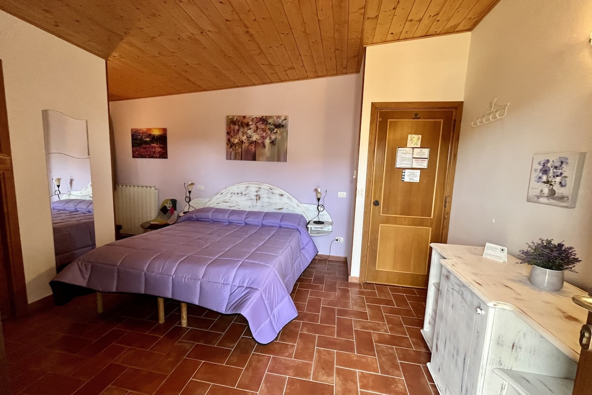 Un dormitorio con cama, mesita de noche, cómoda, una puerta y una pared con un cuadro.