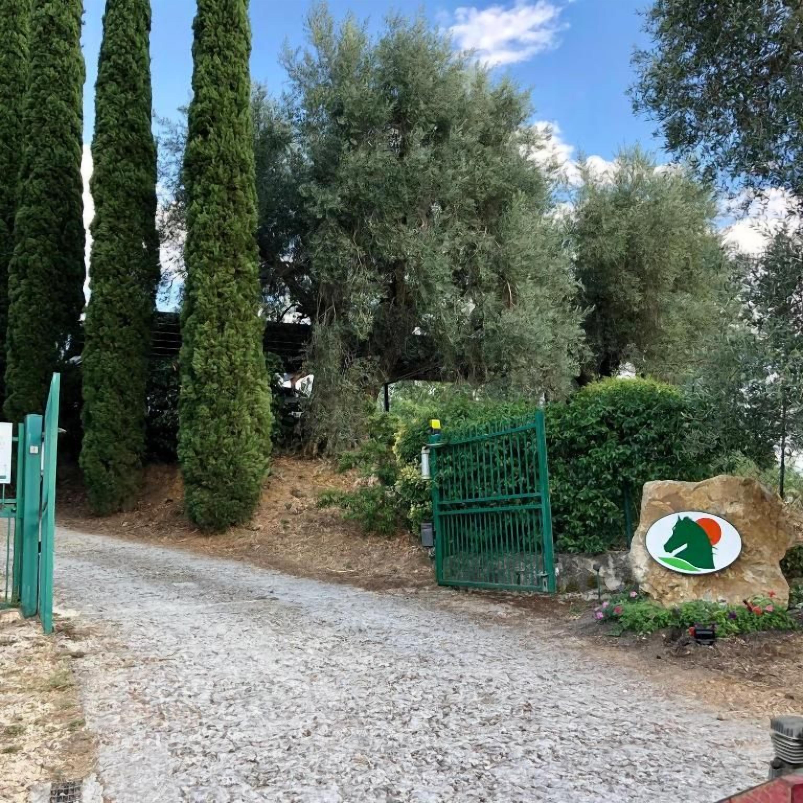Un camino de grava que conduce a una zona vallada con un cartel con la silueta de un caballo.