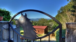 A metal gate with a horse sculpture, a wooden structure in the background, and a mountainous landscape. - Agriturismo Poggio del Drago (Manciano)