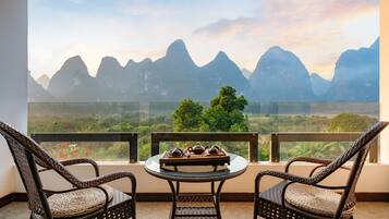 Un balcón con sillas de mimbre y una mesa con teteras, con vistas a un paisaje montañoso.