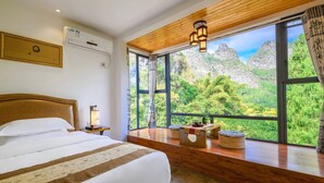 Ein Schlafzimmer mit einem großen Bett, einem Holz-Kopfteil und Blick auf Berge durch große Fenster.