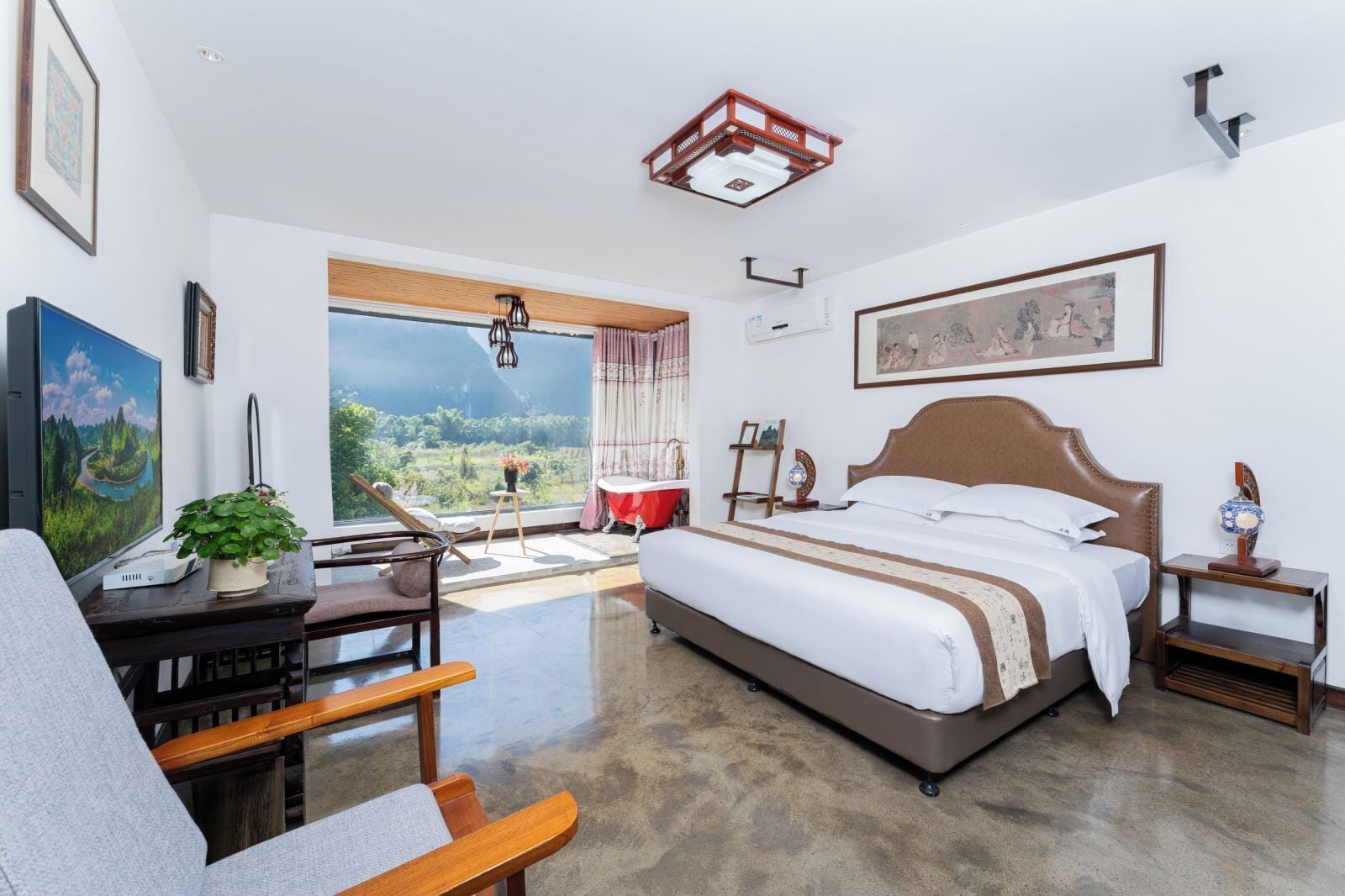 Une chambre spacieuse avec un grand lit, un bureau avec un ordinateur, une chaise, une vue sur l’extérieur et un luminaire au plafond.