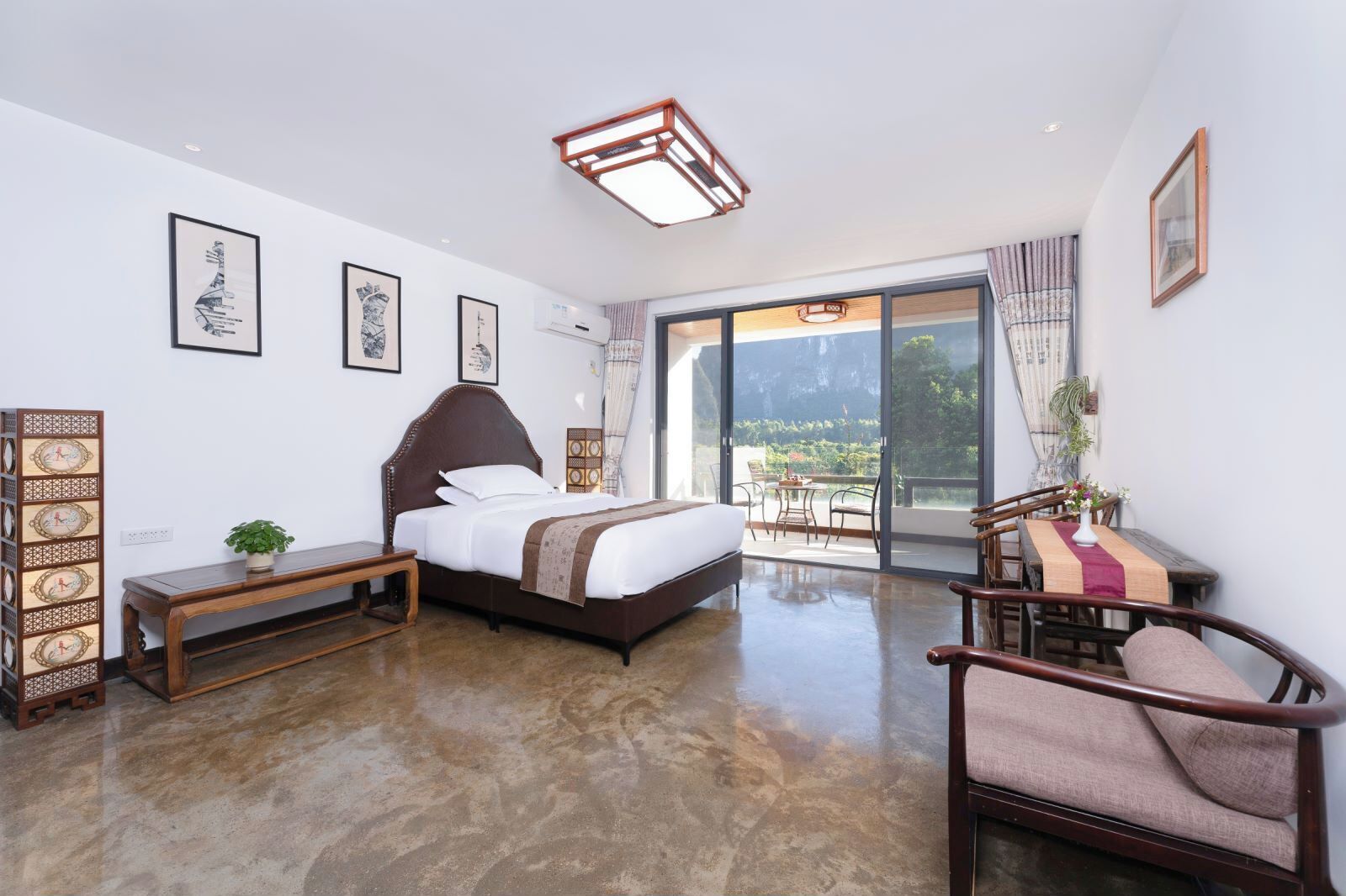 A modern hotel room with a large bed, a wooden bench, a chair, and a balcony with a view.