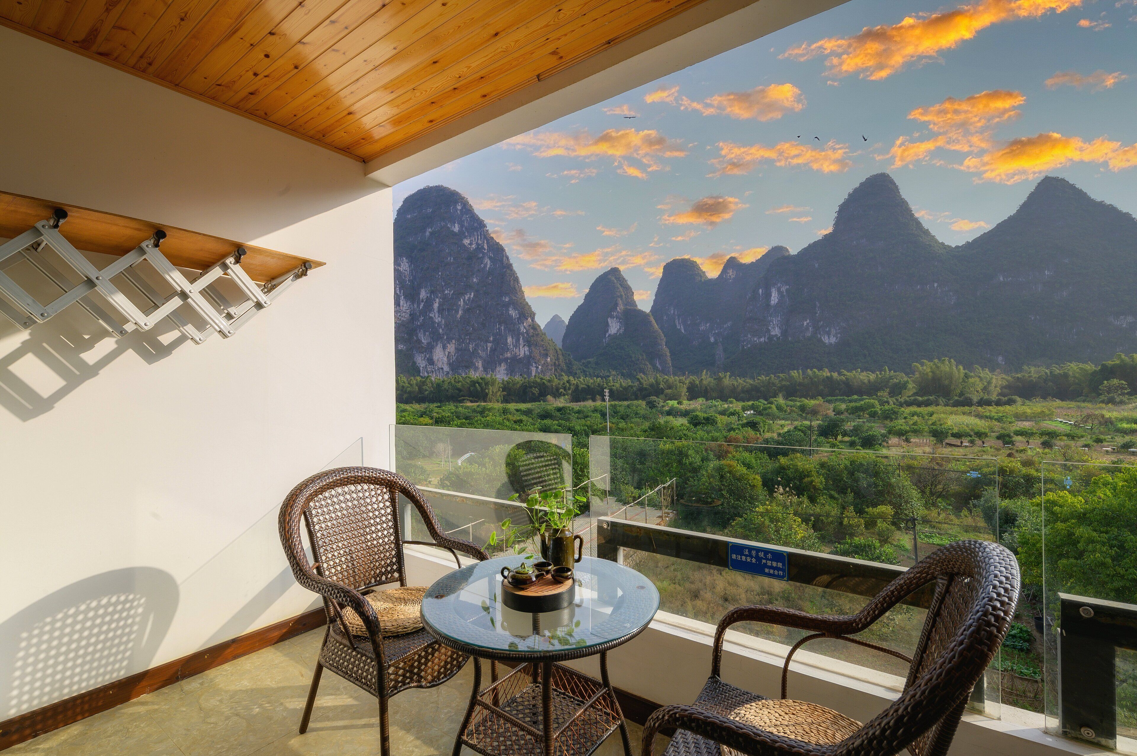 A balcony with wicker chairs, a glass table, and a view of mountains.