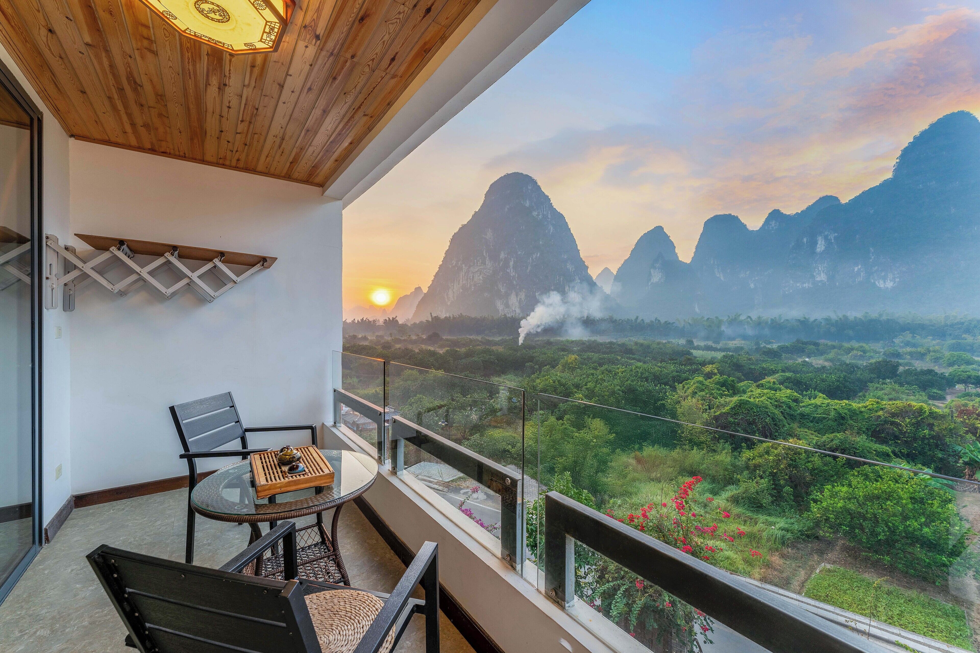 Un balcón con mesa y sillas, con vista a un paisaje montañoso al atardecer.