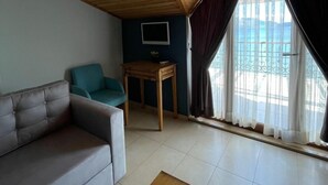 A cozy room with a sloped ceiling, a sofa, a small table, and a window with curtains. - Veziroglu Apart (Datça)