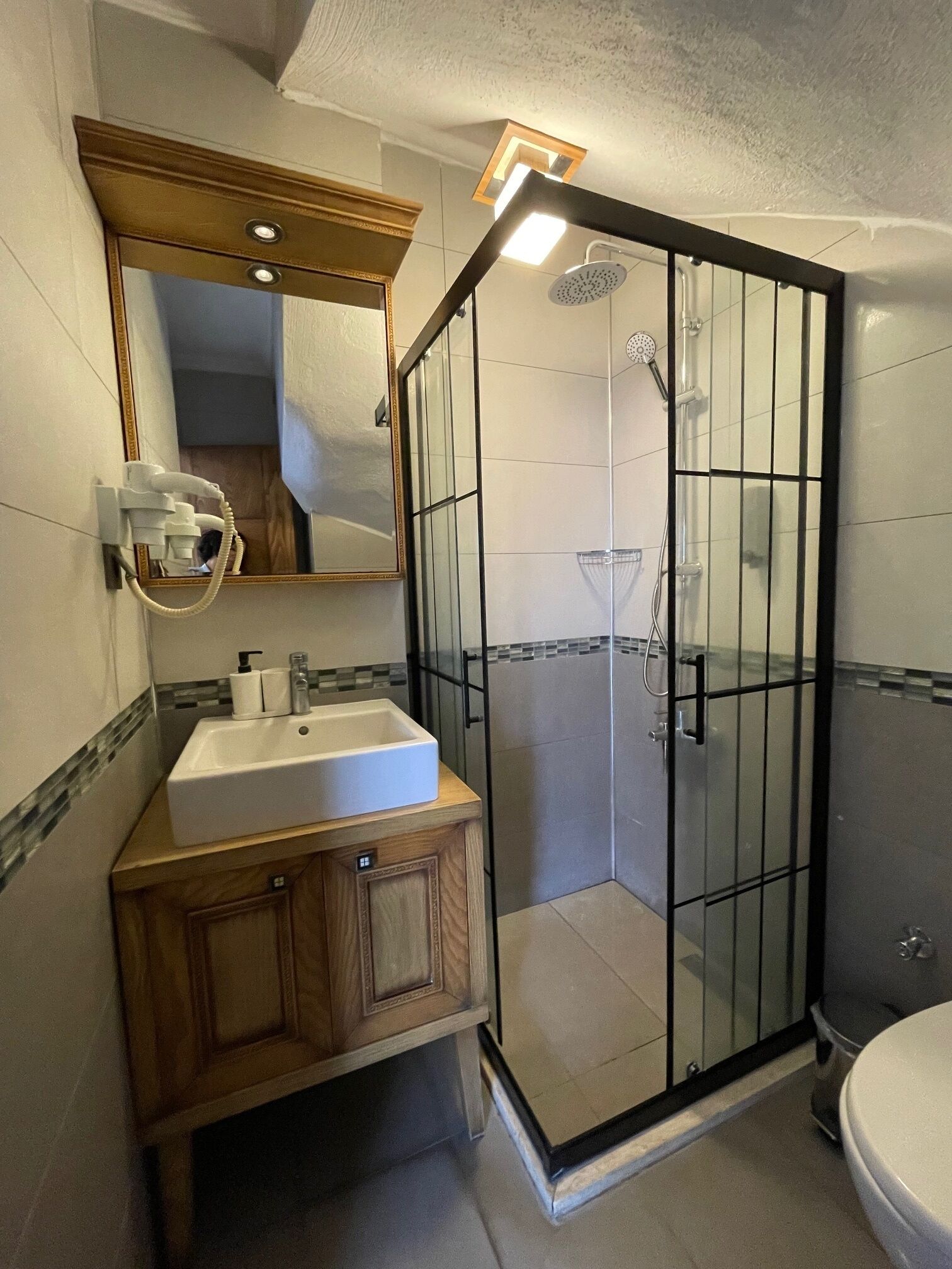 Un baño con ducha de vidrio, tocador de madera con lavamanos y espejo sobre el tocador.