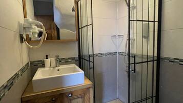 Un baño con ducha de vidrio, tocador de madera con lavamanos y espejo sobre el tocador.