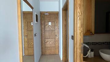 Un pasillo con puertas de madera, suelo de baldosas y un baño con lavabo y espejo.