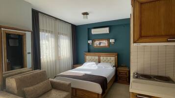 Una camera d'albergo con un letto, un divano, angolo cottura e una finestra con tende.