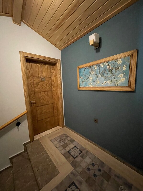 Un pasillo con puerta de madera, suelo de baldosas y un cuadro enmarcado en la pared.