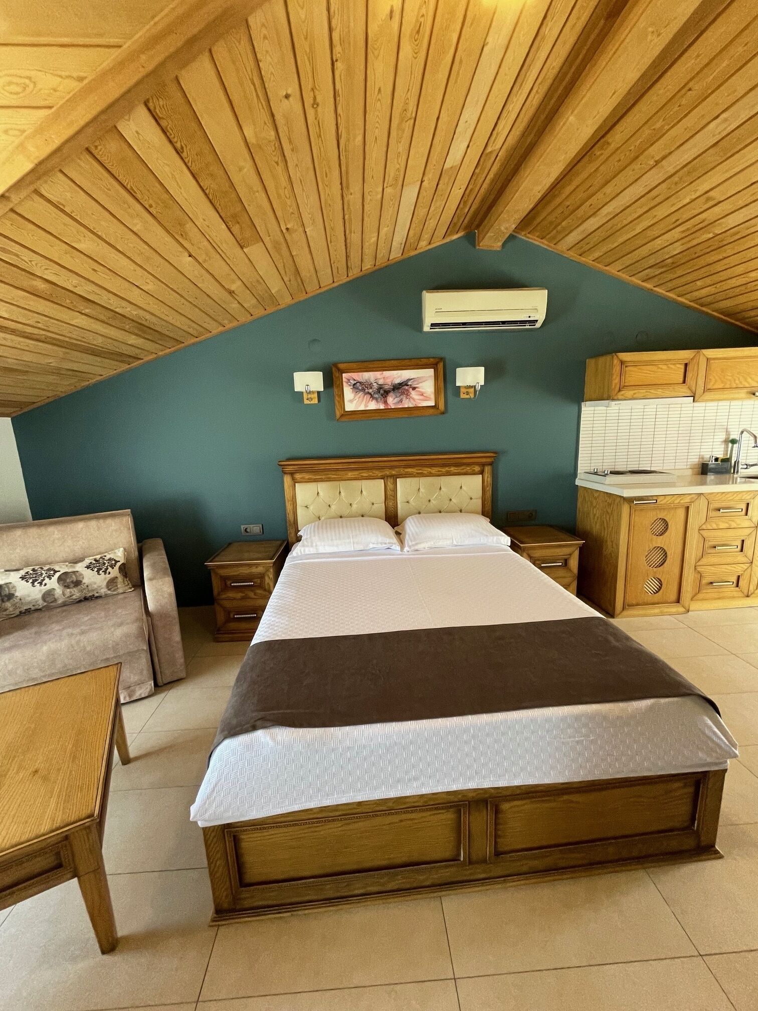 Een slaapkamer met een houten plafond, een bed, een nachtkastje, een dressoir en een kitchenette.