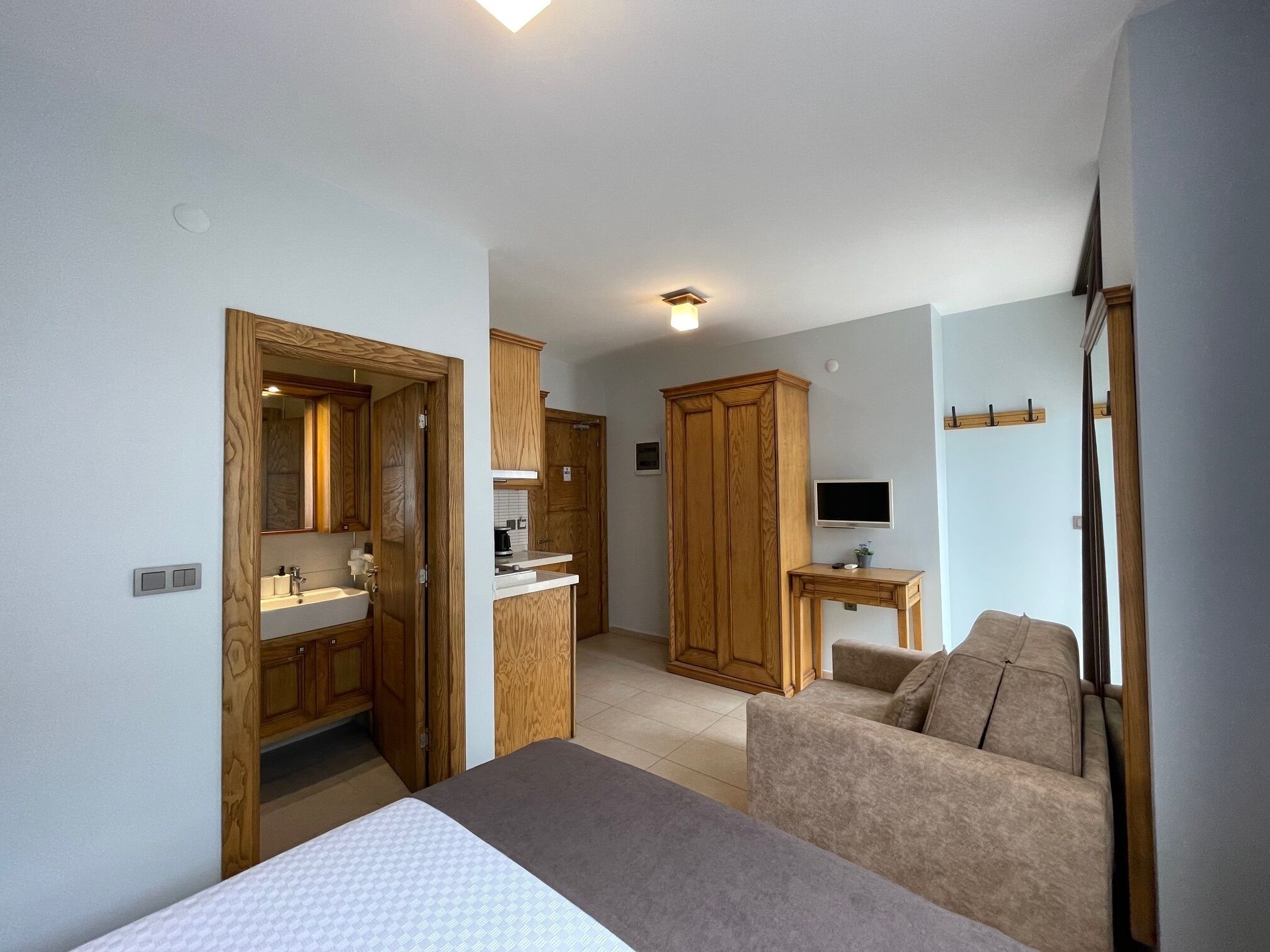Een slaapkamer met een bed, een houten garderobe, een kleine tafel met een televisie en een bank.