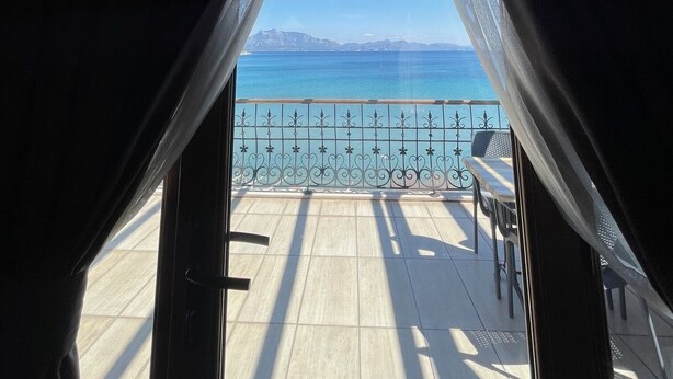 A view from a room with a wooden ceiling and a balcony, overlooking a body of water and distant mountains. - Veziroglu Apart (Datça)