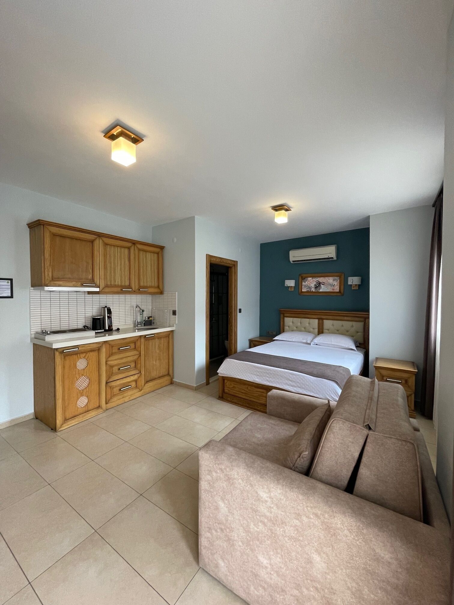 A compact room with a kitchenette, a bed, and a sofa.